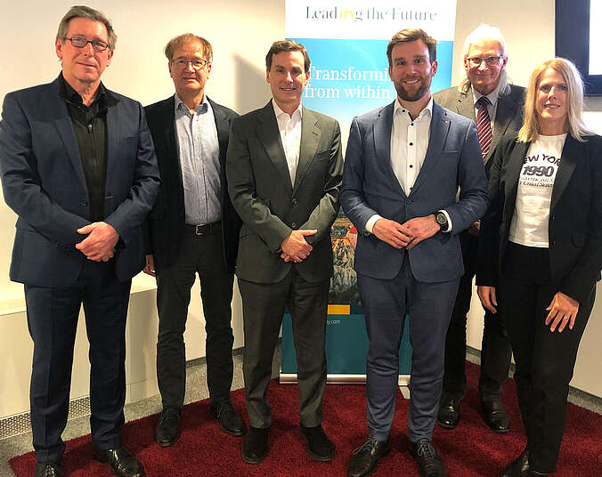 Fünf Männer und eine Frau stehen vor dem Firmen-Rollup