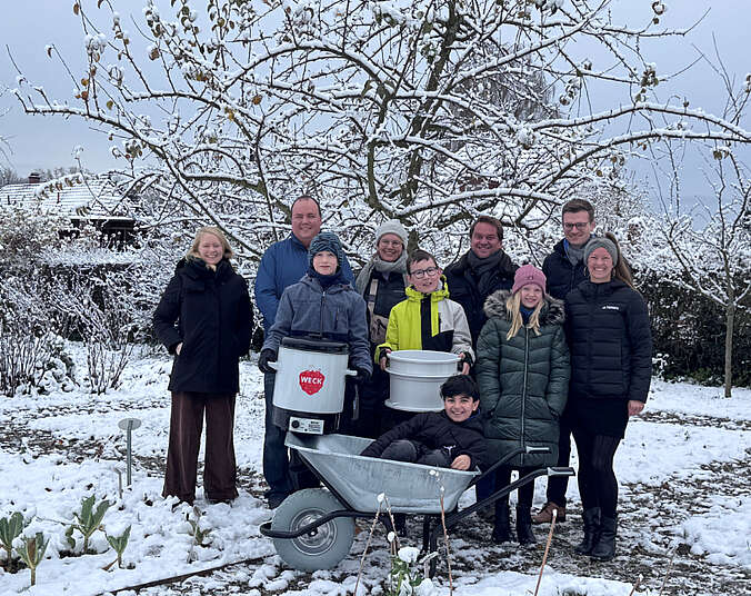 Männer, Frauen und Kinder vor verschneiten Bäumen mit einer Schubkarre