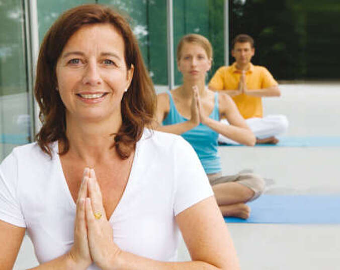 Zwei Frauen und ein Mann sitzen im Schneidersitz beim Yoga.