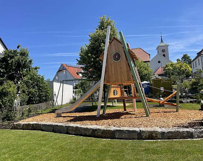 Spielplatz mit Häusern und Kirchturm im Hintergrund