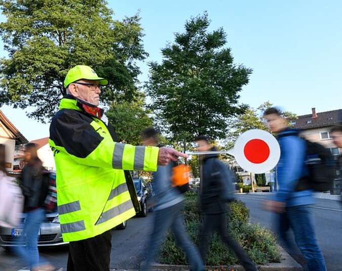 Mann mit Warnkelle lässt Personen Straße überqueren