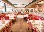 Eingedeckte Tische mit rot-weiß karierten Sitzmöbeln im rustikalen Restaurant des Hotel Gerbe.