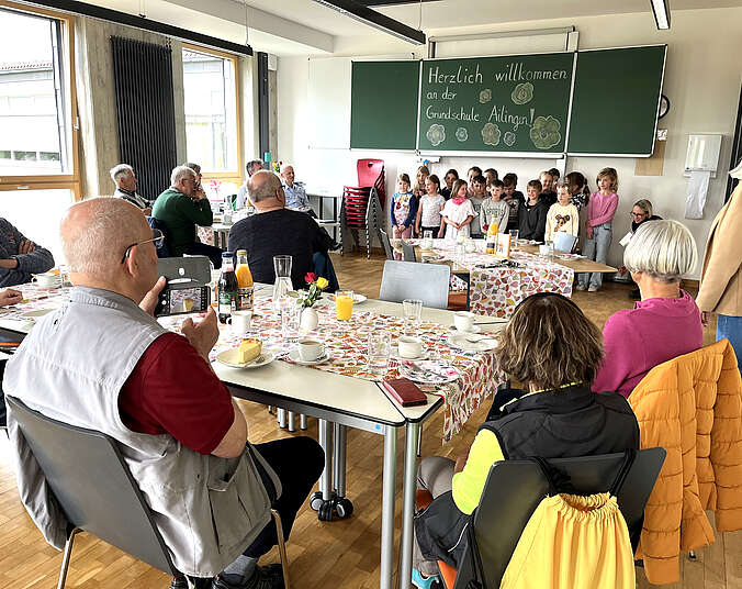 Raum mit Personen an Tischen und einer Kindergruppe