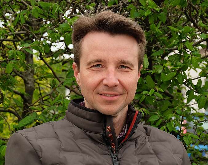 Portraitbild Mann vor grüner Hecke