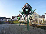 Spielplatz mit großer Sandgrube und zwei großen Klettertürmen, im Hintergrund Häuser