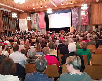 Personen sitzen in Stuhlreihen in einer Halle