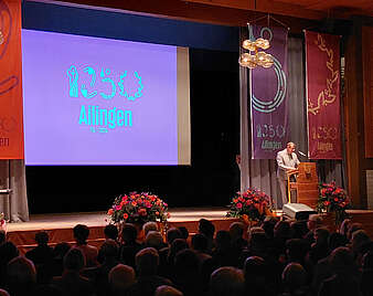 Blick auf eine Bühne in einer Halle mit Logo und Fahnen im Hintergrund