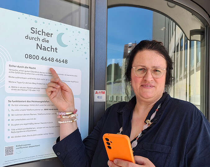 Eine Frau mit Handy in der Hand zeigt auf Plakat